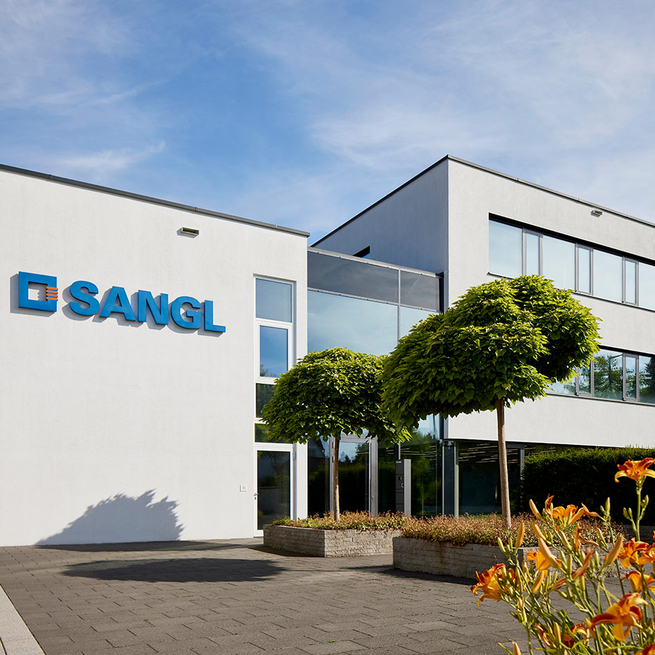 Hauptgebäude der Firma Sangl mit Logo und blühender Gartenanlage im Vordergrund
